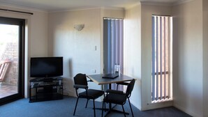 A small room with a TV on a stand, two chairs, a table, and a window with blinds. - Arkana Motor Inn & Terrace Apartments (Mount Gambier)