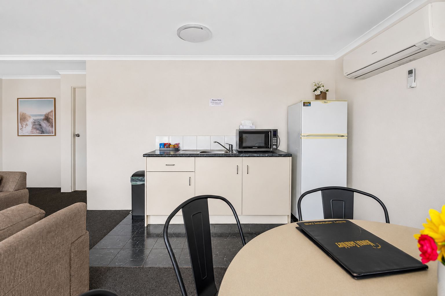 Habitación de hotel compacta con kitchenette, comedor con mesa y sillas, y una cama al fondo.