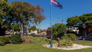 A flagpole with the Australian flag, surrounded by landscaped garden beds and trees. - Arkana Motor Inn & Terrace Apartments (Mount Gambier)