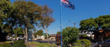 A flagpole with the Australian flag, surrounded by landscaped garden beds and trees.