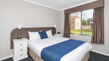 A hotel room with a bed, bedside tables, a window with curtains, and a view of the outside.