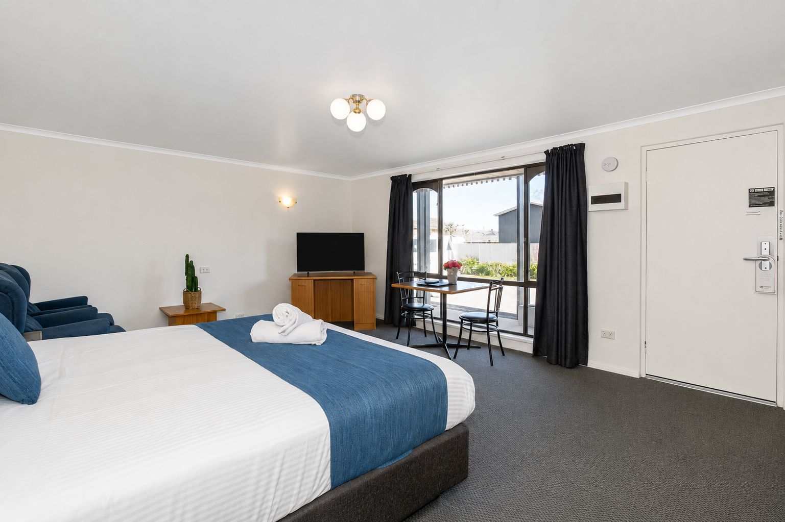 A hotel room with a bed, a desk, a television, and a view of the outside.