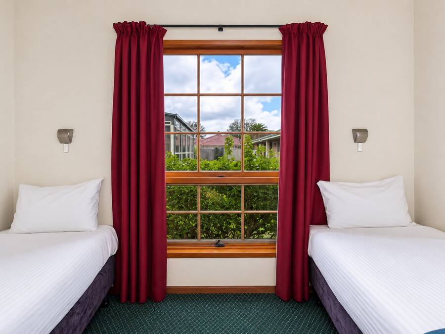 A hotel room with two beds, a large window with curtains, and a view of a residential area.