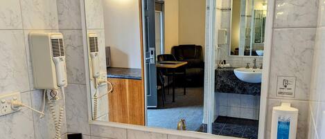 A bathroom with a white sink, marble tiles, a mirror, a hairdryer, and a hand soap dispenser.