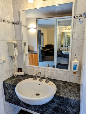 A bathroom with a white sink, marble tiles, a mirror, a hairdryer, and a hand soap dispenser. - Arkana Motor Inn & Terrace Apartments (Mount Gambier)