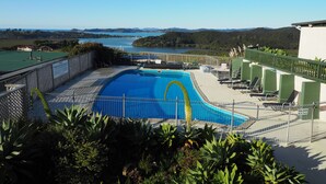 Piscina con vista a un lago y montañas, rodeada de sillones de descanso y una zona vallada.