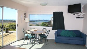 Una habitación con vista a la playa, un sofá azul, una mesa con sillas y un televisor montado en la pared.