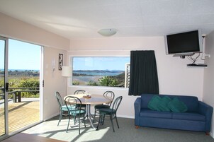 A room with a view of a beach, a blue sofa, a table with chairs, and a TV mounted on the wall.