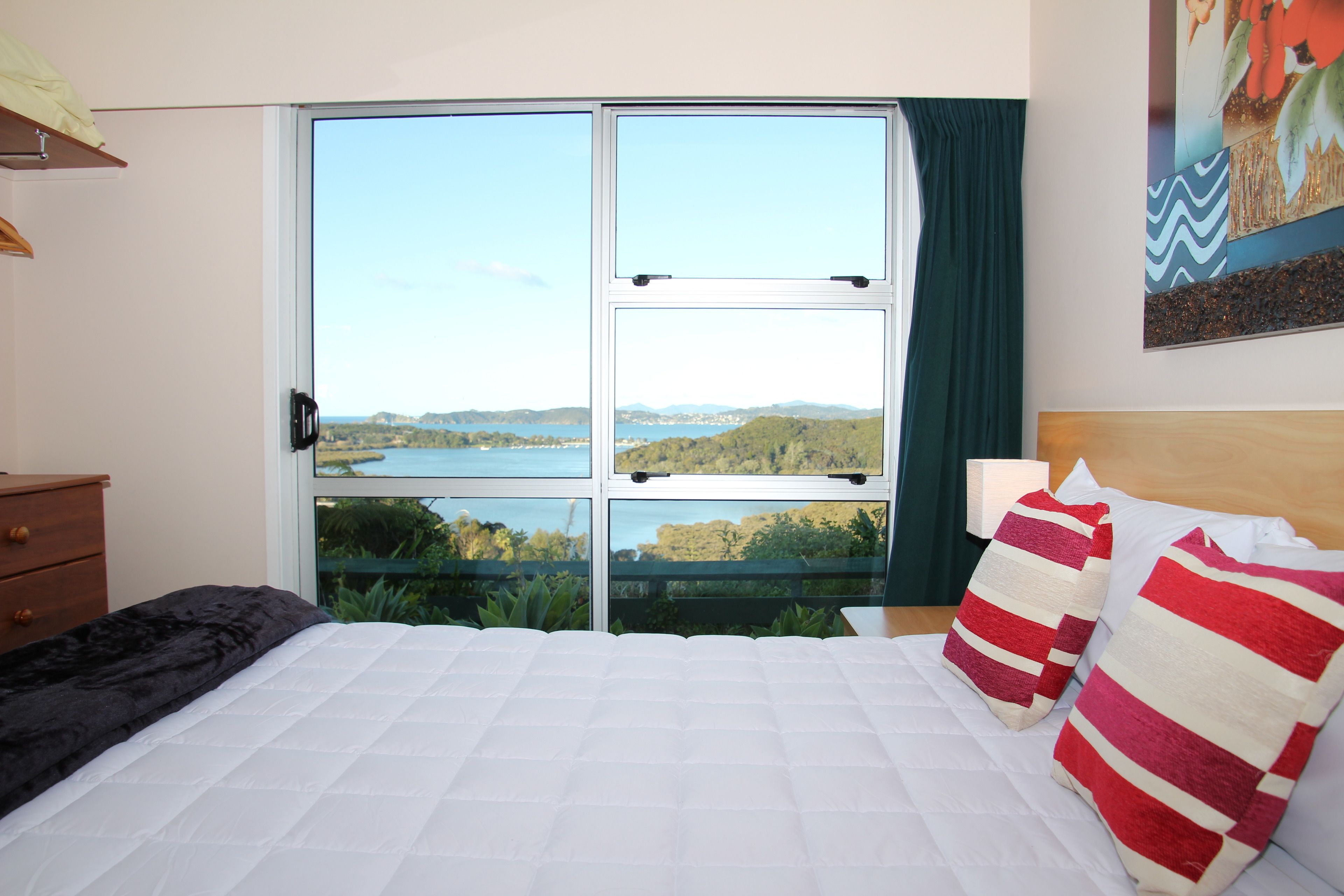 A bedroom with a large window offering a scenic view of a lake and hills.