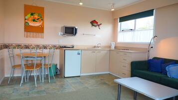Cocina compacta con refrigerador, microondas y lavamanos. Hay un comedor con sillas y mesa, y un sofá verde en la sala.