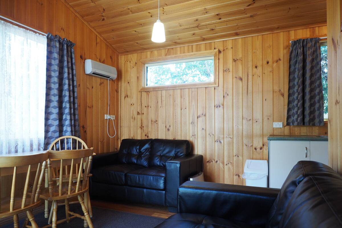 Een houten cabin inrichting met een bank, een eettafel met stoelen en een kleine kitchenette.