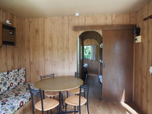 Une pièce de taille modeste, avec un intérieur en bois, une table ronde entourée de chaises, un canapé à motifs et une porte donnant sur un autre espace.