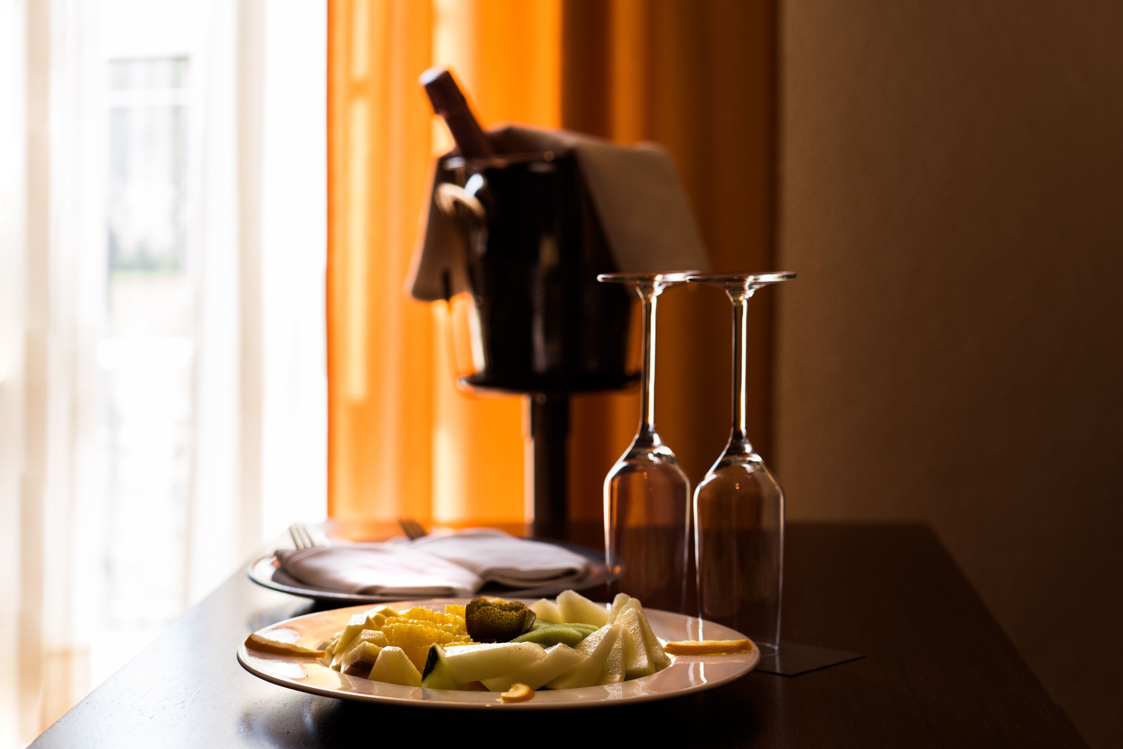 A dining table with a plate of food, two empty wine glasses, and a bottle of wine.