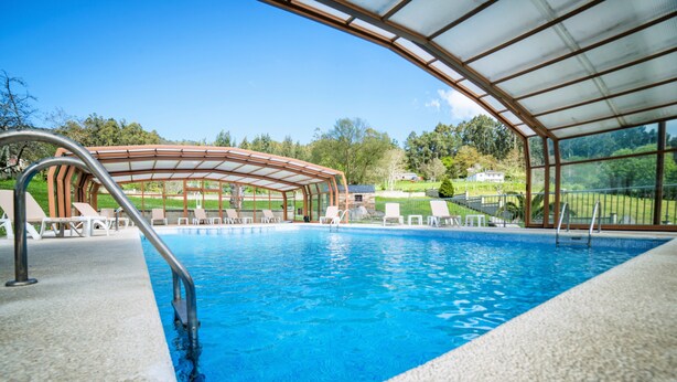 Ein Schwimmbecken mit überdachtem Bereich, klarem blauen Wasser und Blick auf die umliegende Landschaft.