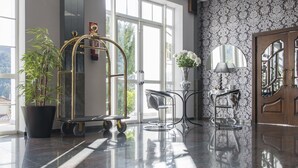 Eine moderne Lobby mit einer großen Topfpflanze, einem goldfarbenen Aufzug und einer Sitzecke mit einem Blumenarrangement.