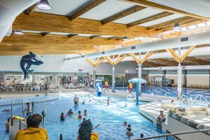Une piscine intérieure dotée de plusieurs couloirs, surveillée par des maîtres-nageurs et ornée d’une sculpture de dauphin.