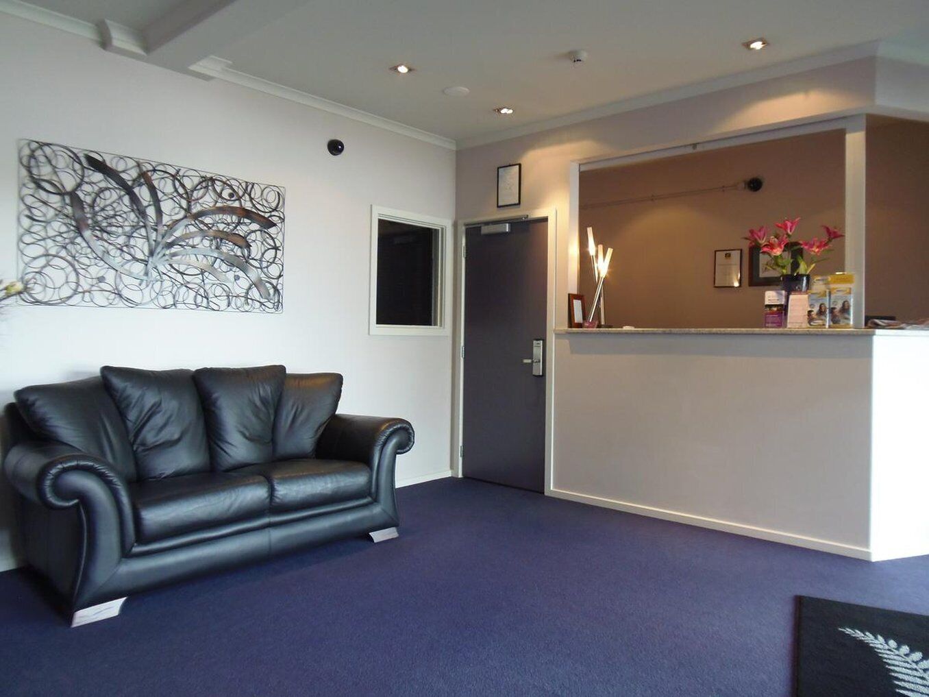 A reception area with a black leather sofa, a modern abstract art piece, and a reception desk with a vase of flowers.