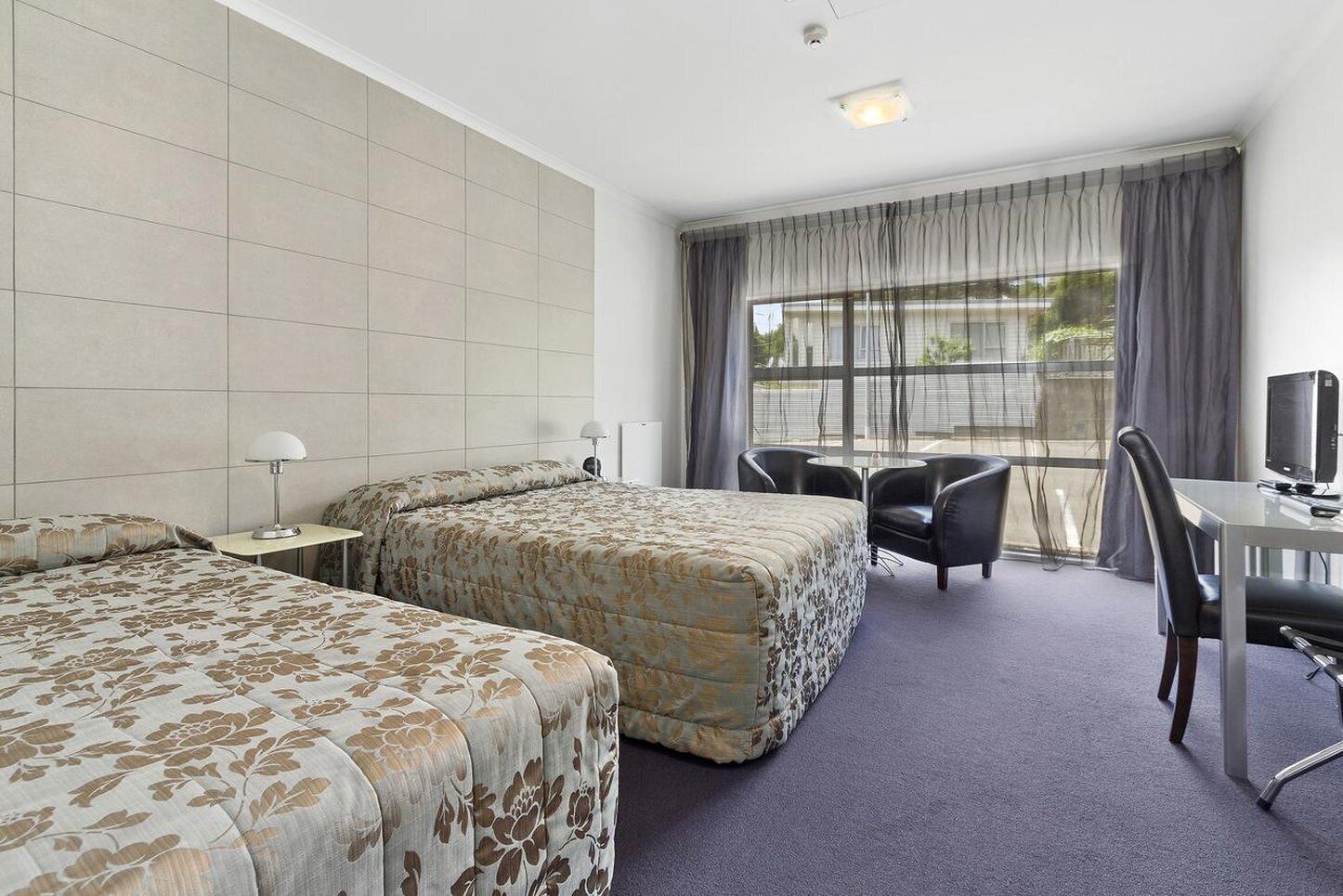 A hotel room with two beds, a desk with a computer, and a chair.