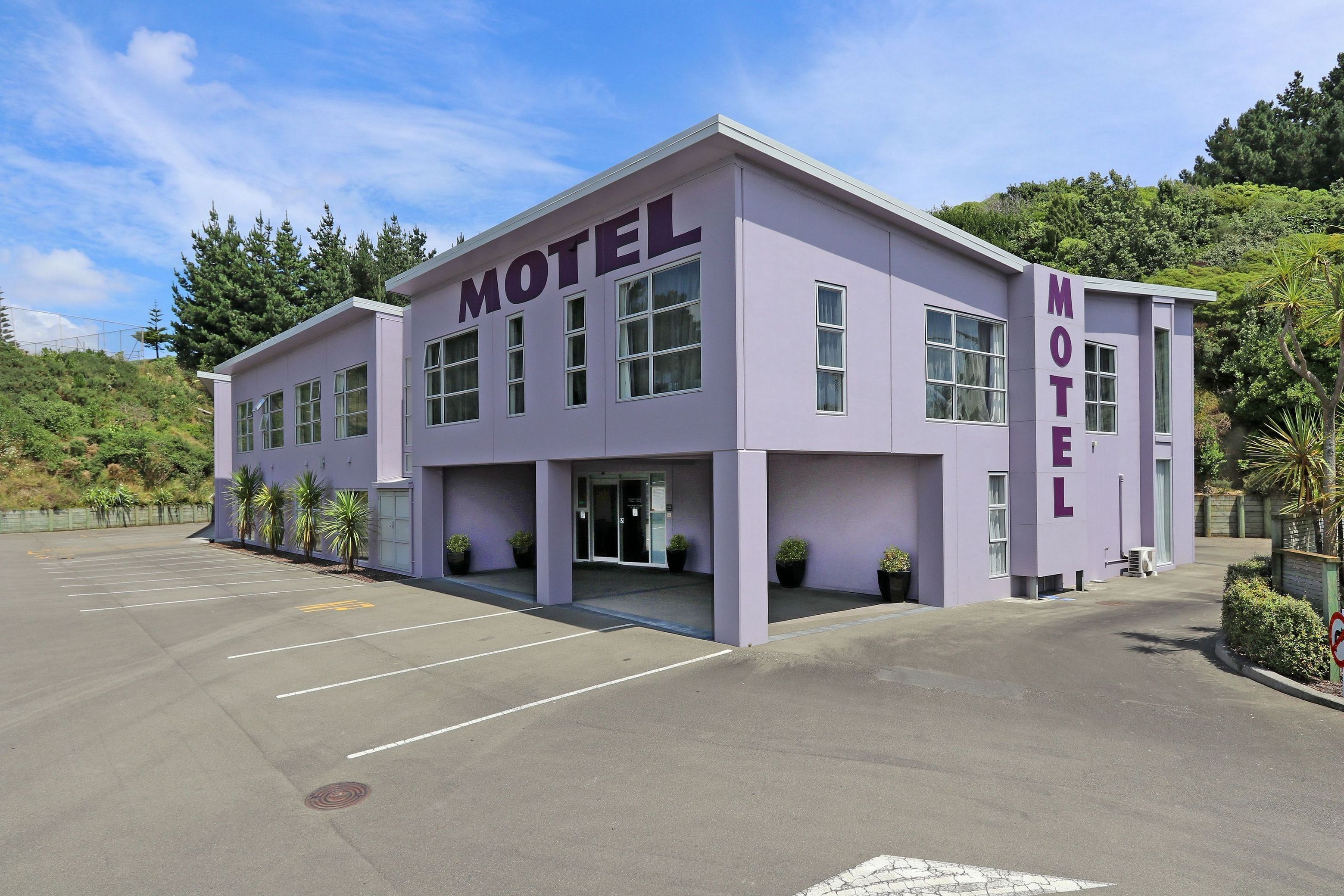 A motel with a flat roof, large windows, and a parking lot.