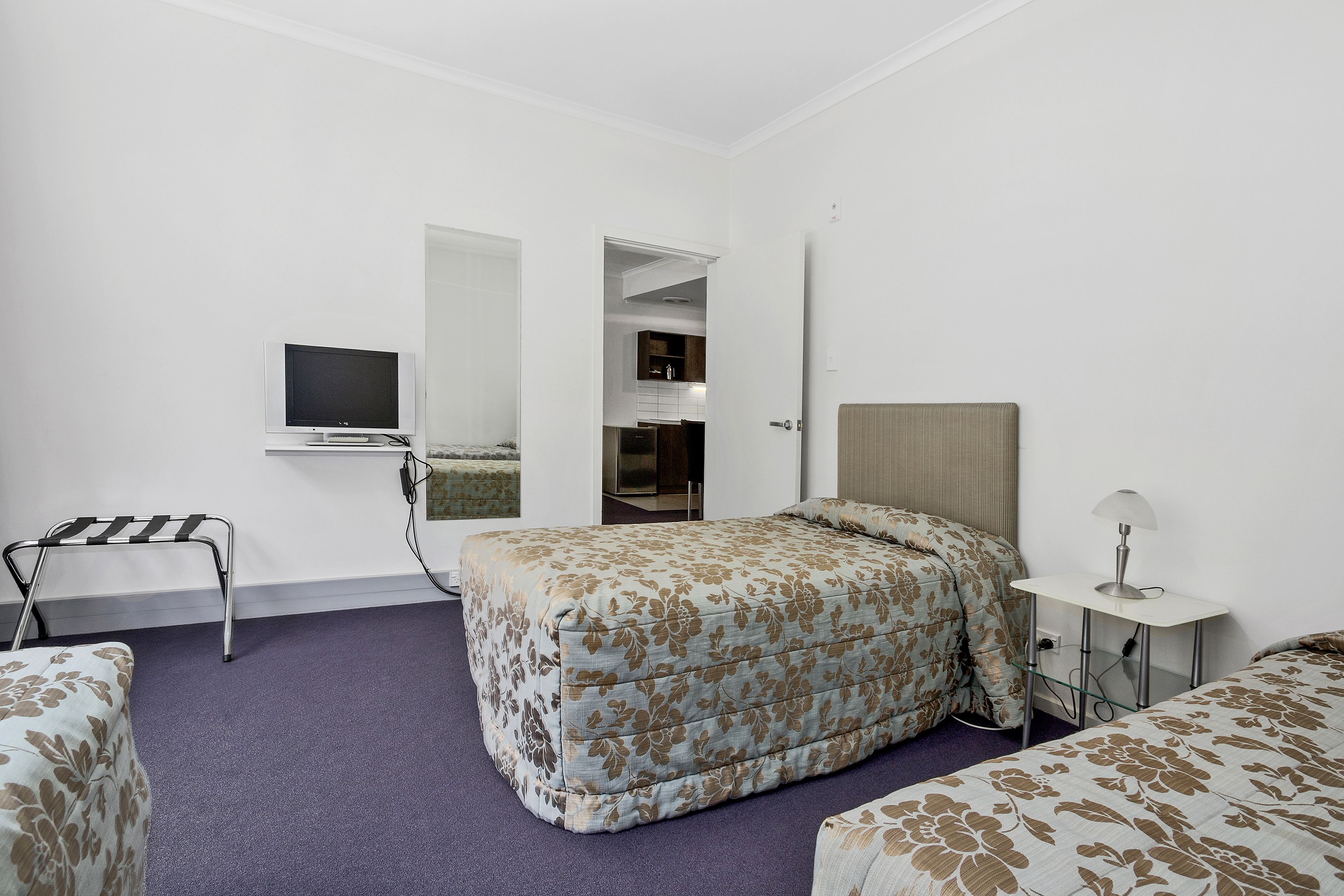 Quarto de hotel com cama, escrivaninha, cadeira, televisão e banheiro visível por uma porta aberta.