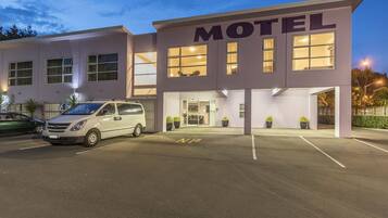 Een motel met een bord met de tekst MOTEL boven de ingang. Er staan potplanten voor het gebouw en een witte bestelwagen staat op de parkeerplaats.