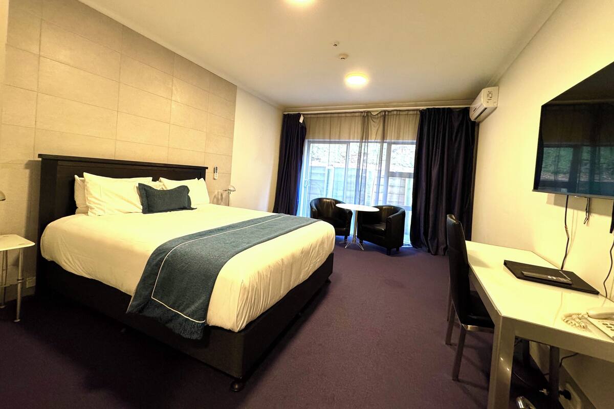 A hotel room with a large bed, a desk, a chair, a television, and a window with curtains.