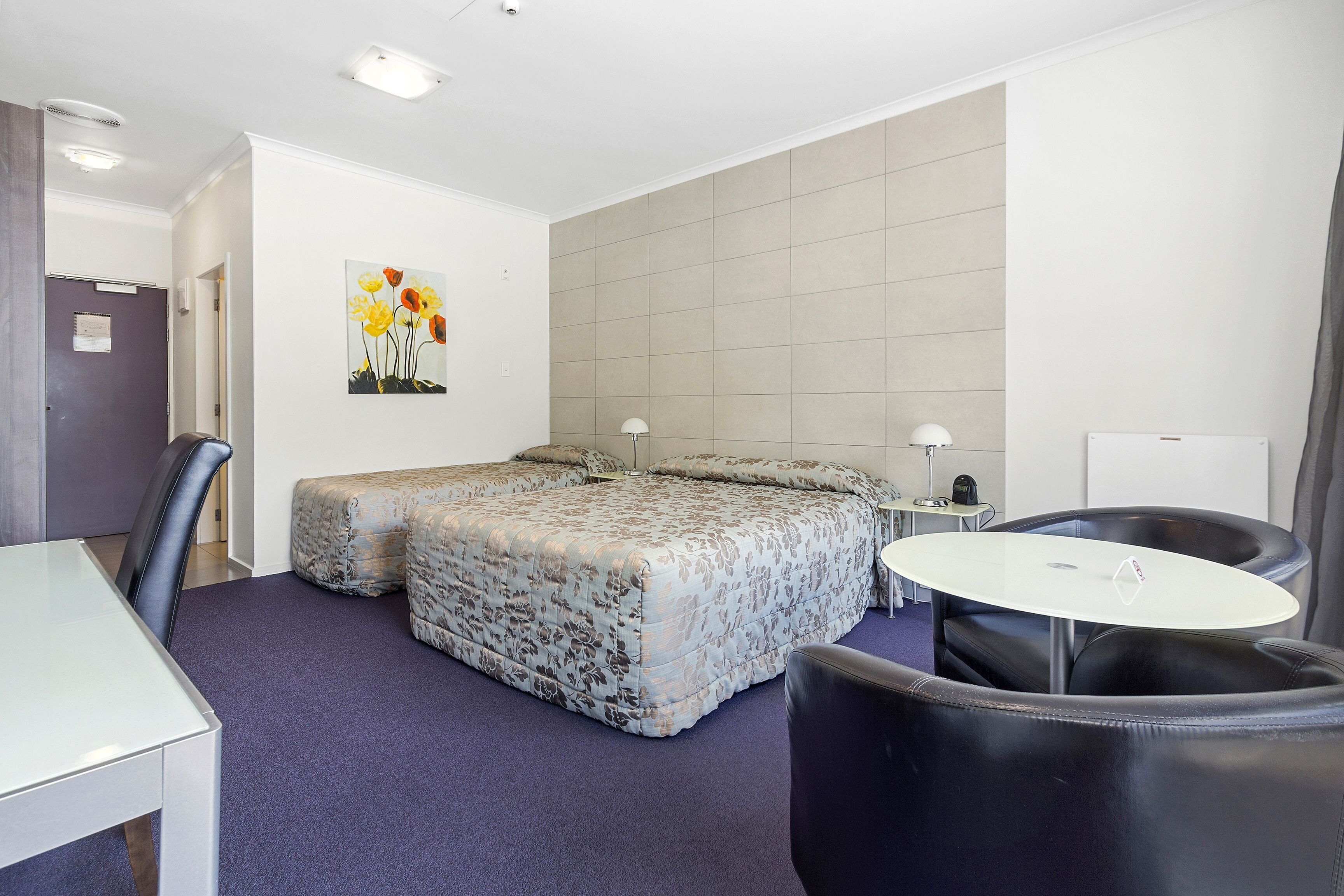 Una habitación de hotel con una cama, dos sillas, una mesita y un cuadro en la pared.