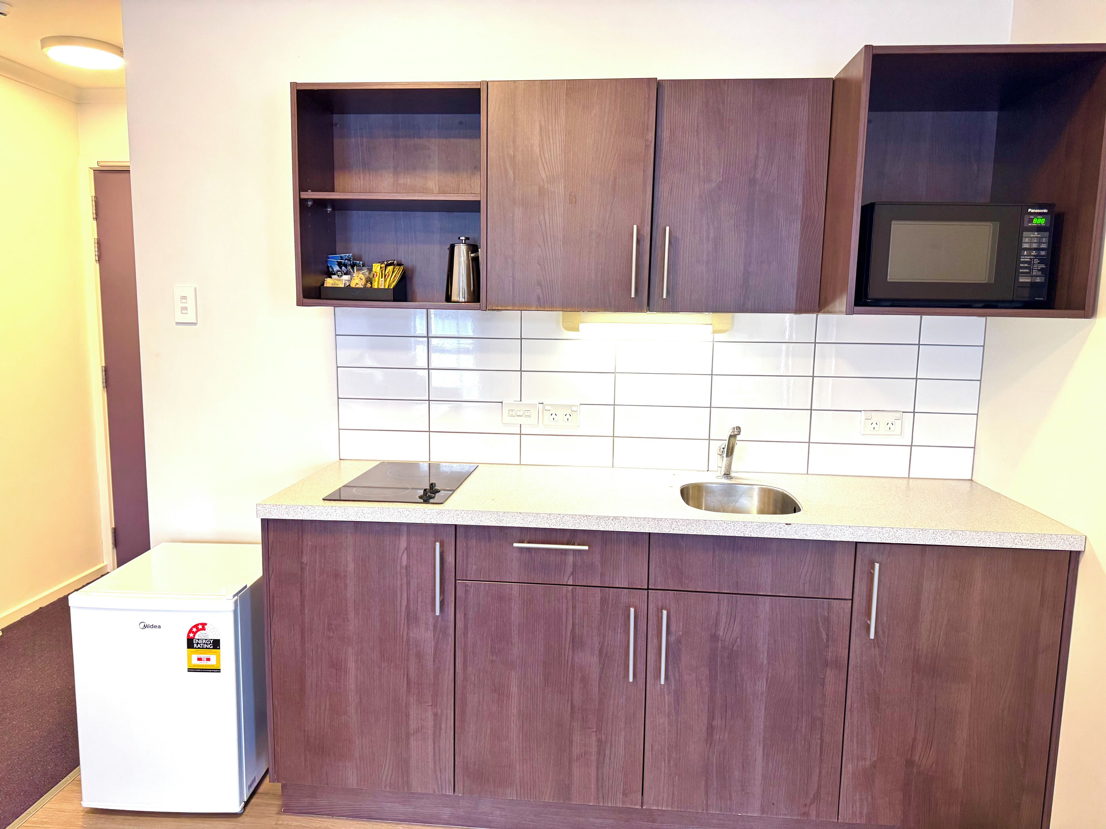 A compact kitchen with wooden cabinets, a microwave, a sink, and a small refrigerator.