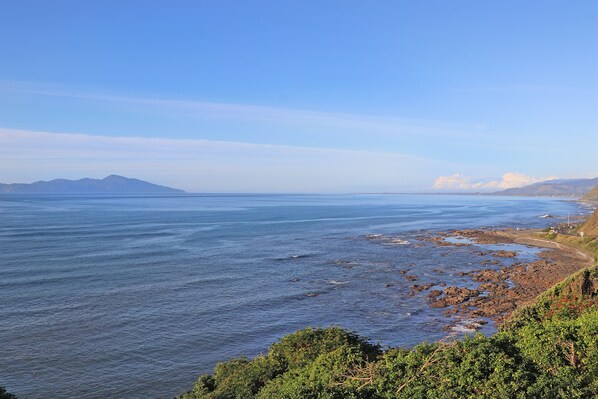 A coastal landscape with a rocky shoreline, clear blue sky, and distant mountains.