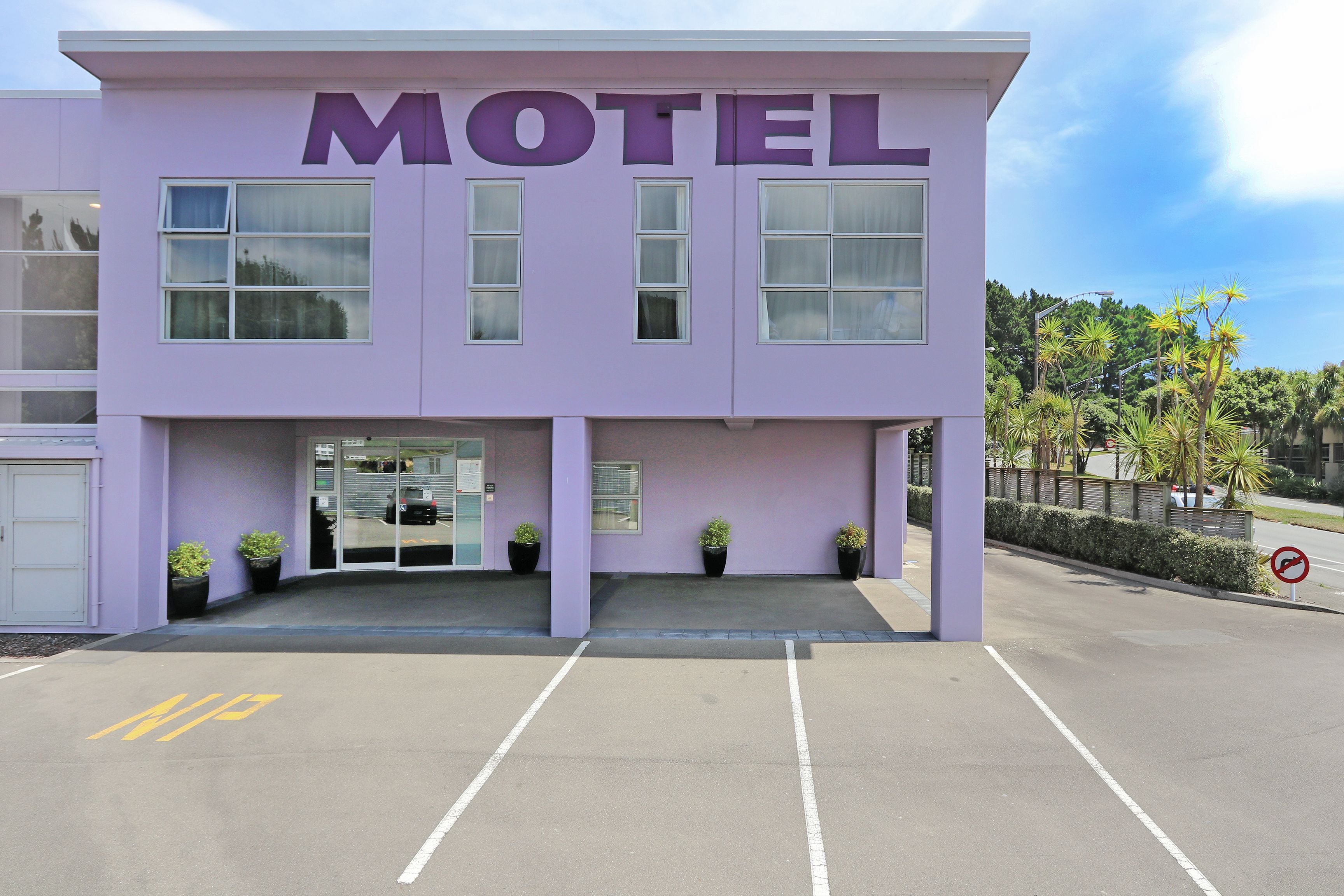 A motel with a purple facade, large windows, and a parking lot.