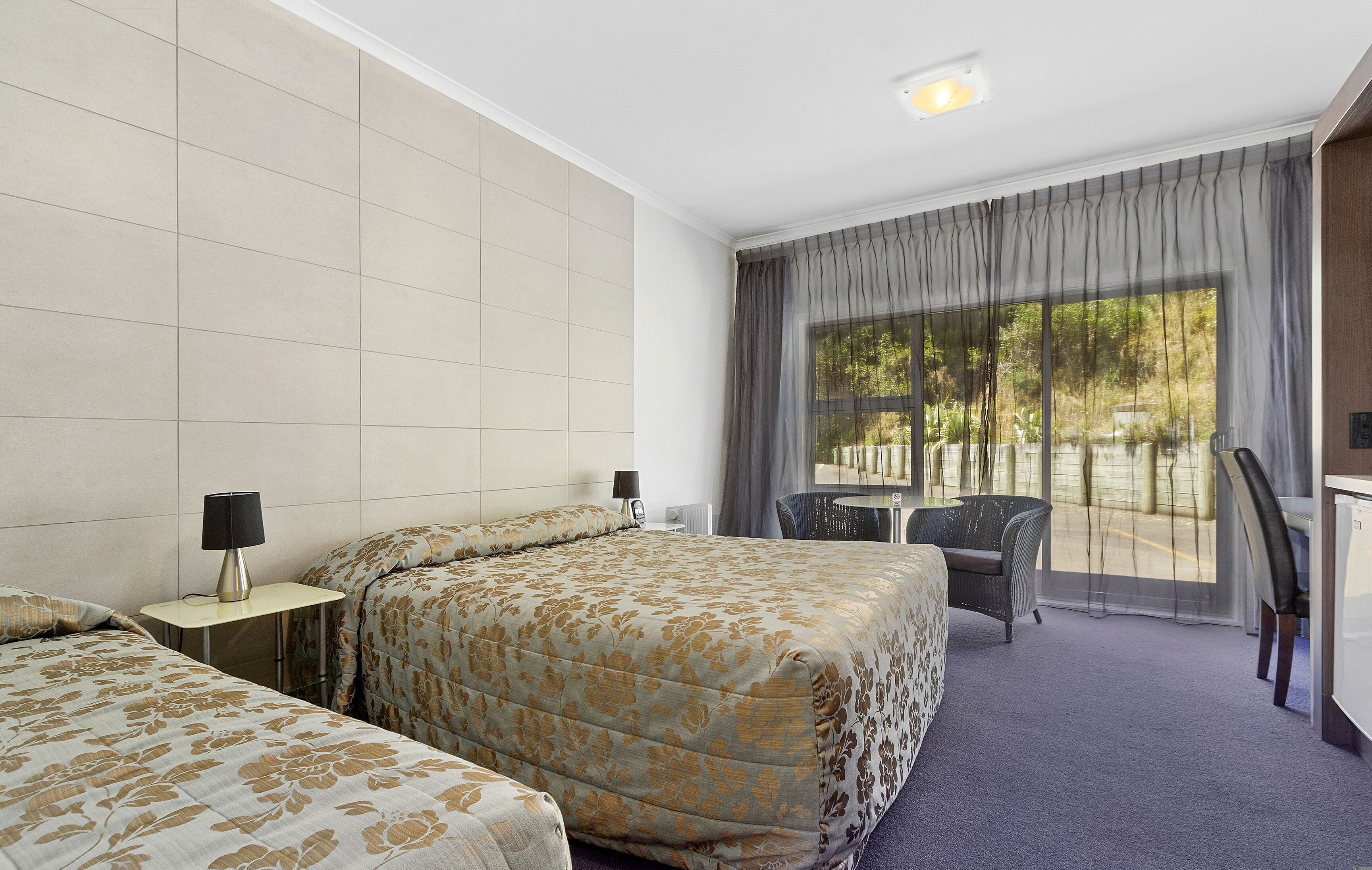 A hotel room with two beds, a desk, a chair, and a view of the outdoors.
