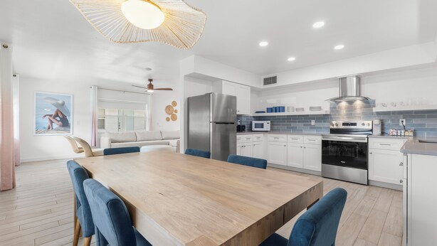 A modern kitchen with white cabinets, stainless steel appliances, and a wooden dining table.