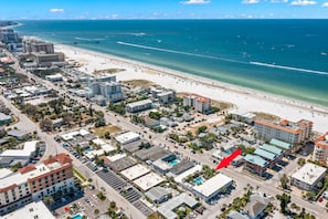 An aerial view of a coastal city with a beachfront, buildings, and a red arrow pointing to a hotel.