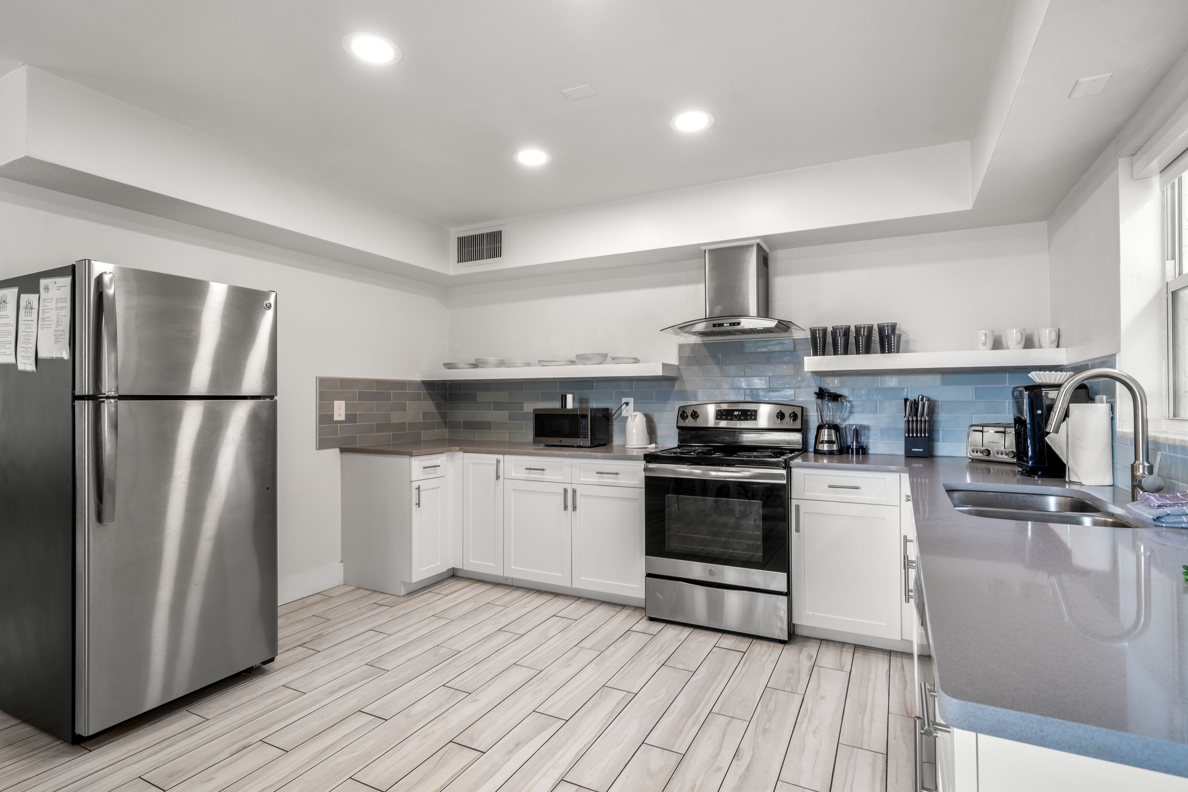 A modern kitchen with stainless steel appliances, white cabinetry, and a grey countertop.