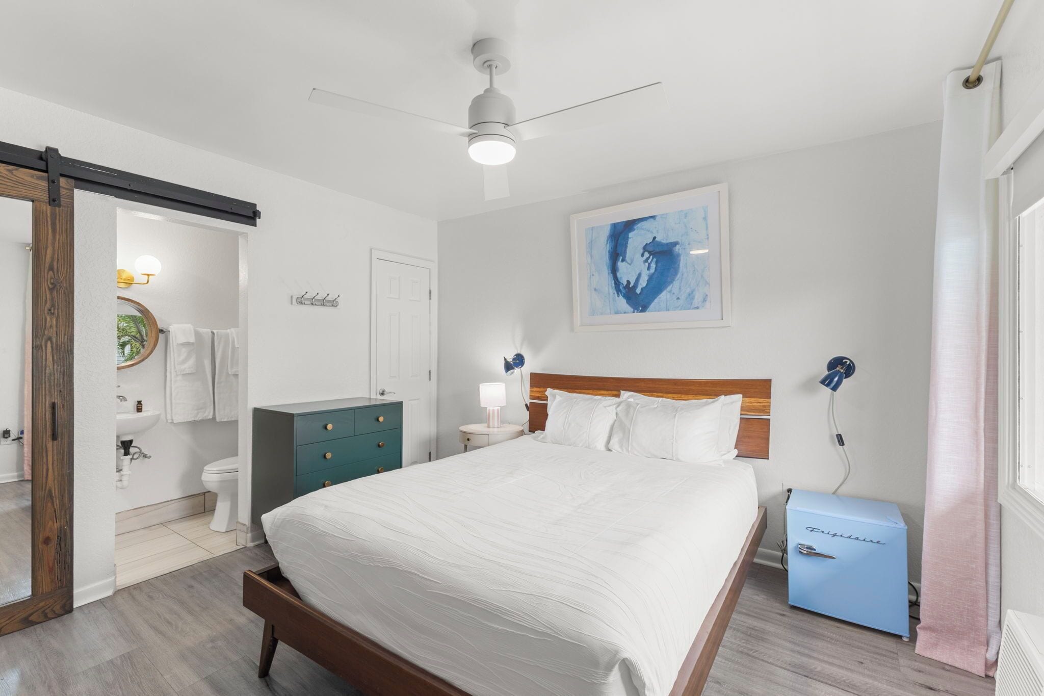 A bedroom with a bed, a dresser, a nightstand, a ceiling fan, a wall-mounted lamp, and a small blue cabinet.