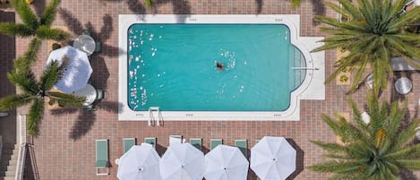 Oversigtsbillede af en swimmingpool omgivet af palmer og udendørs møbler med parasoller.