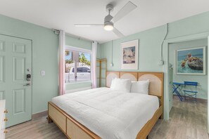 A bedroom with a bed, a ceiling fan, a window with a view of the street, and a door. - Hotel Cabana Clearwater Beach (Clearwater Beach)