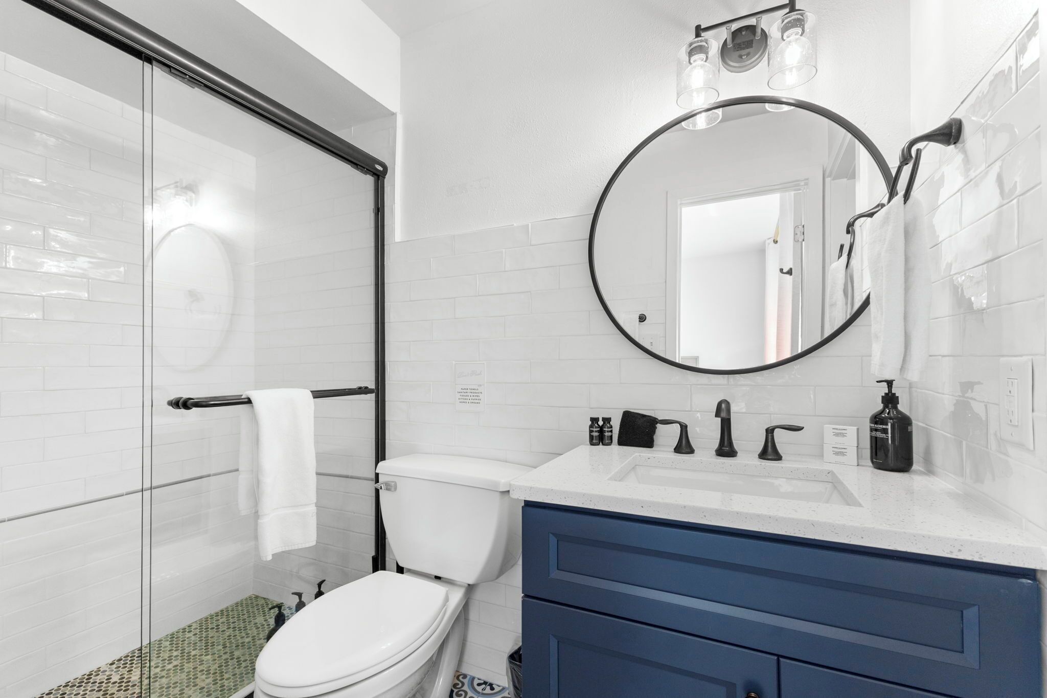 A modern bathroom with a glass shower enclosure, a white toilet, a sink with a mirror above it, and a blue vanity.