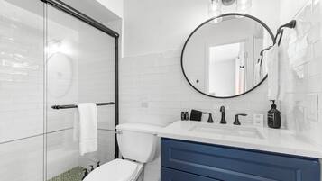A modern bathroom with a glass shower enclosure, a white toilet, a sink with a mirror above it, and a blue vanity.