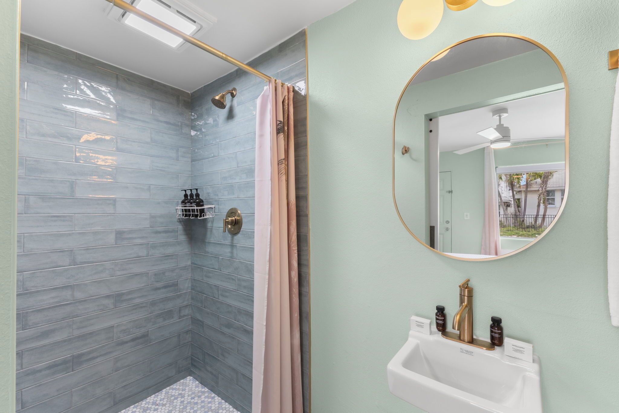 Een badkamer met een douche, wastafel met spiegel en toiletartikelen.