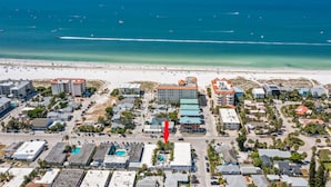An aerial view of a coastal town with a beach, buildings, and a parking lot.