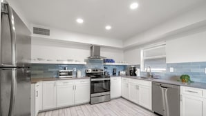 A modern kitchen with white cabinets, stainless steel appliances, and a blue-tiled backsplash. - Hotel Cabana Clearwater Beach (Clearwater Beach)
