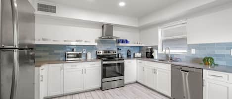 Una cocina moderna con armarios blancos, electrodomésticos de acero inoxidable y salpicadero de azulejos azules.