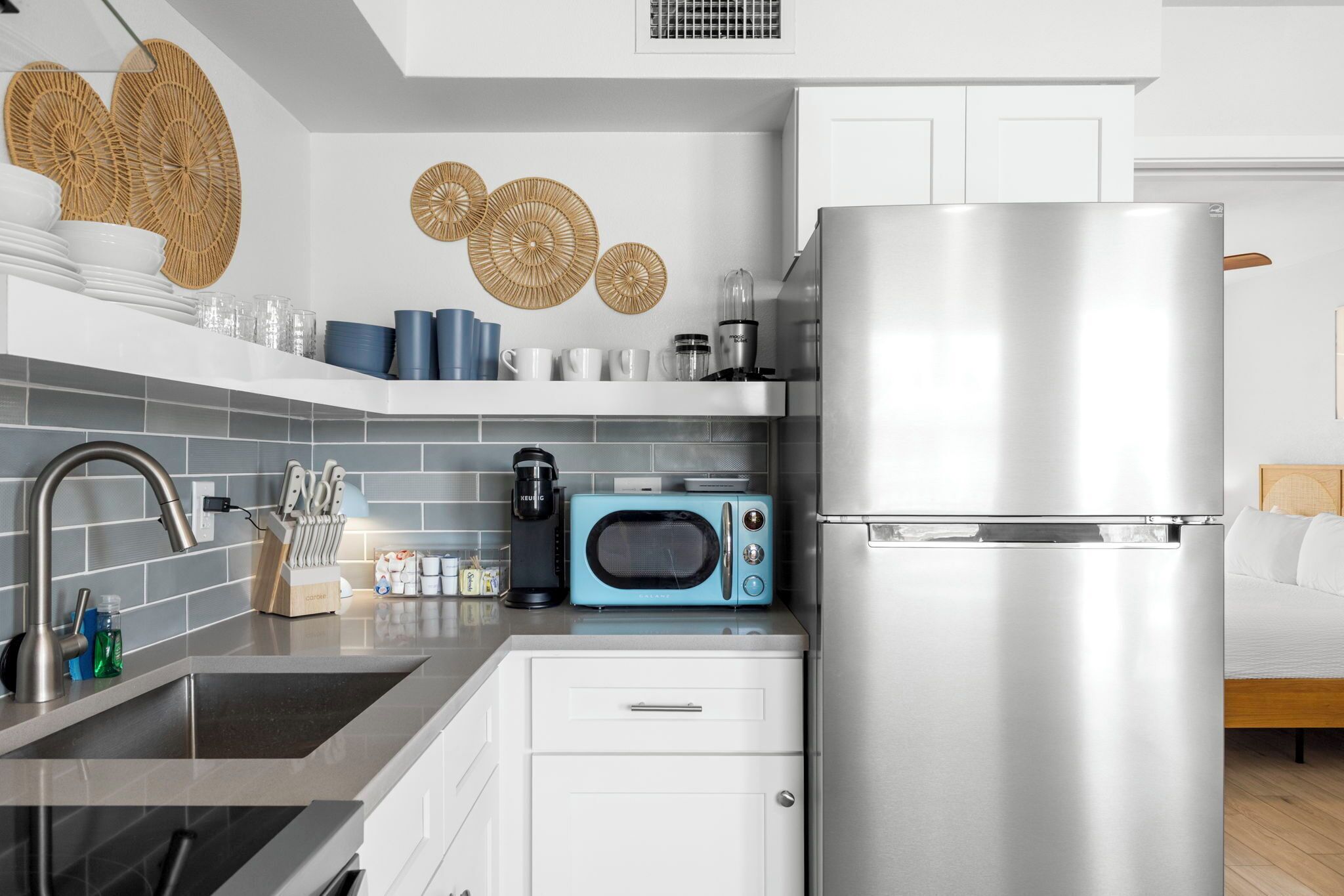 A modern kitchen with a stainless steel refrigerator, a blue microwave, and a sink with a modern faucet.