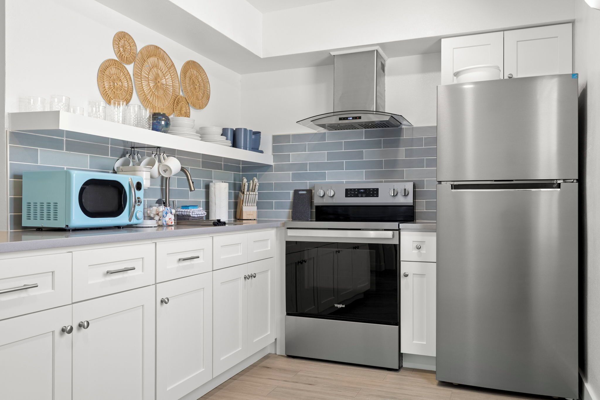 A modern kitchen with white cabinets, a stainless steel refrigerator, a microwave, an oven, and a range hood.