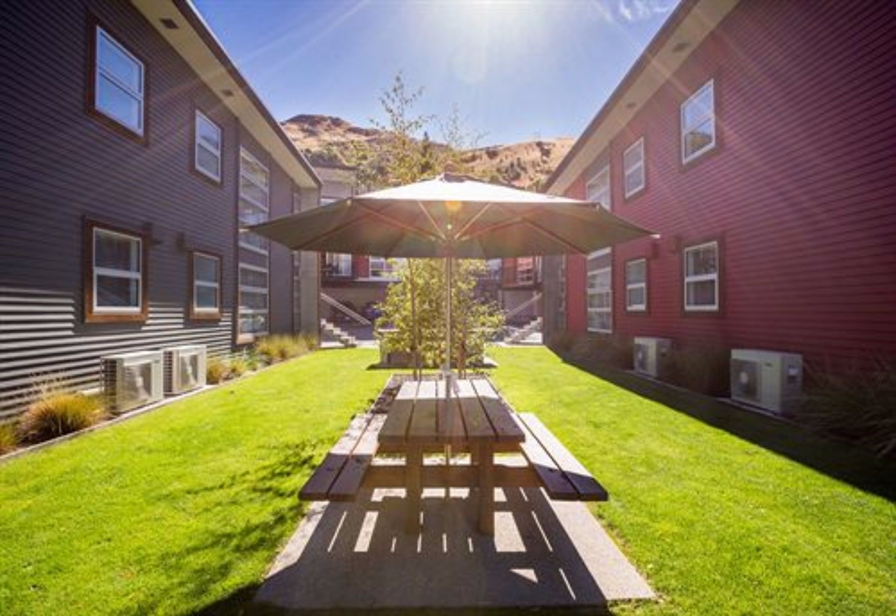 Un patio con mesa de picnic y sombrilla, rodeado de edificios.