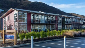 A modern building with large windows and a balcony, surrounded by greenery and a parking lot. - Marina Apartments Element Escapes (Queenstown)