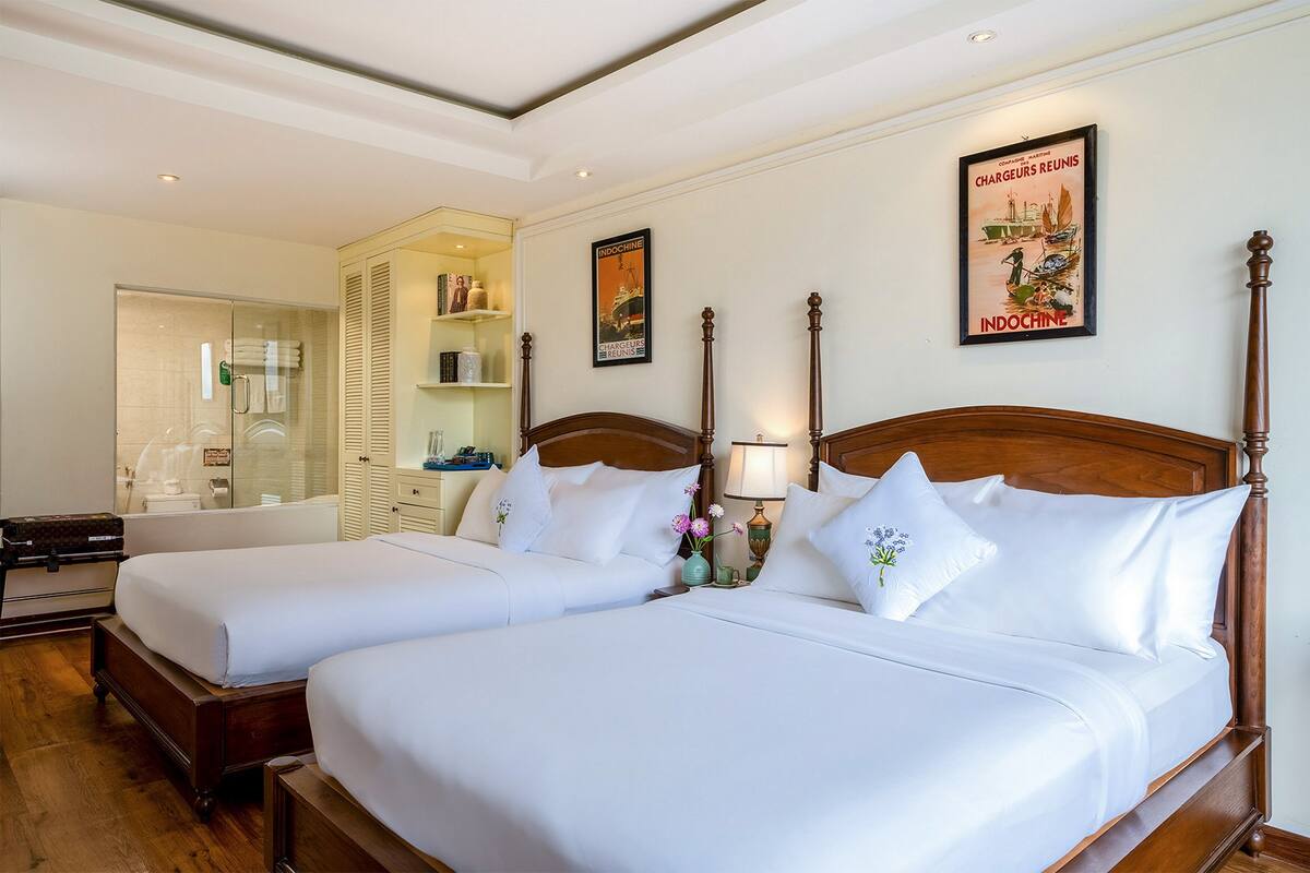 A hotel room with two beds, a bathroom, and a wooden headboard.