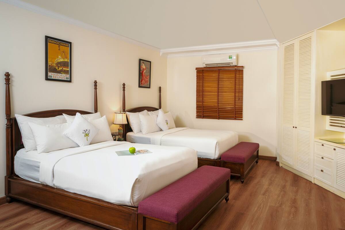 A hotel room with two single beds, a bench, a television, and a wardrobe.