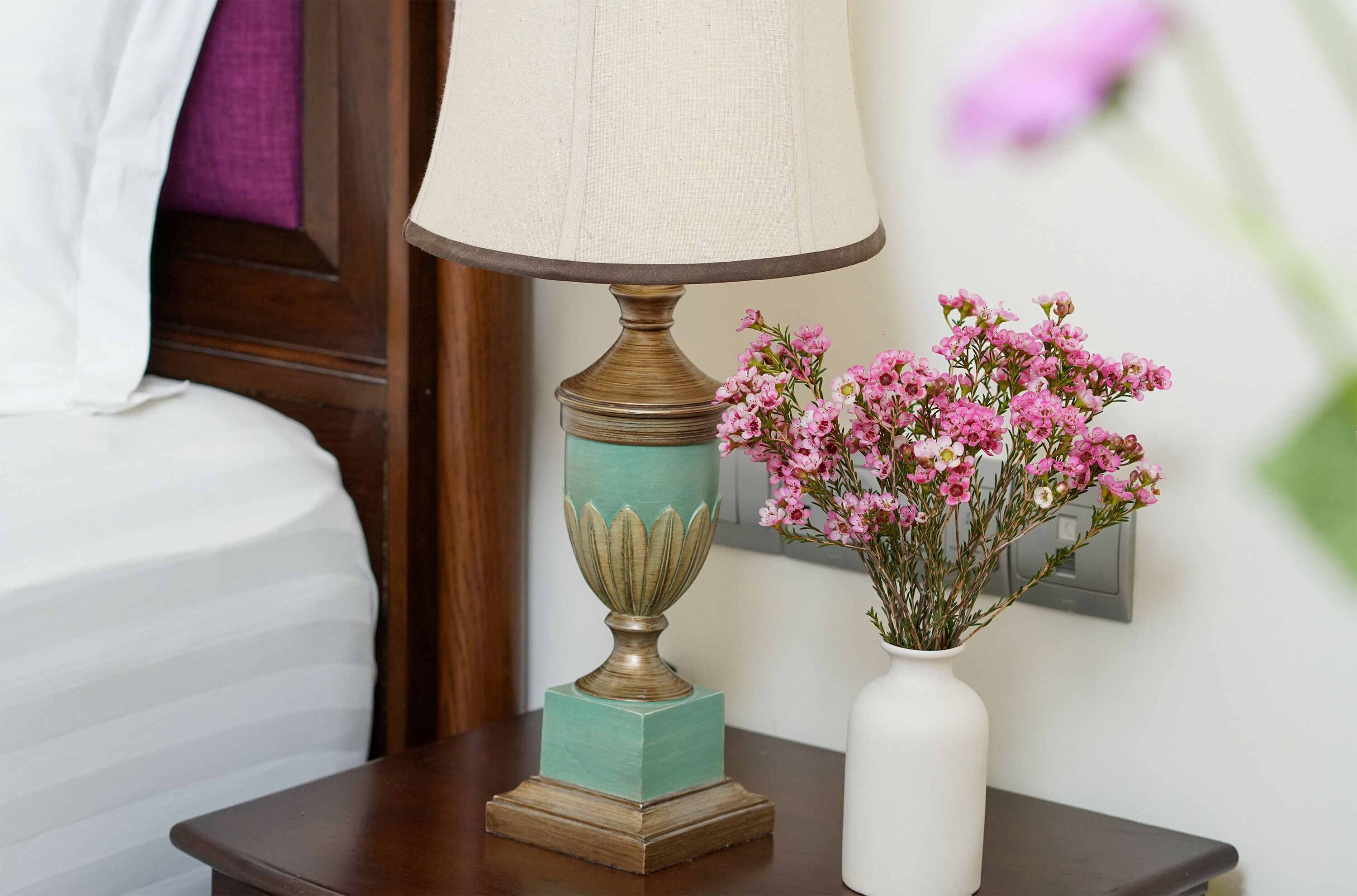 A bedside table with a lamp and a vase of flowers.